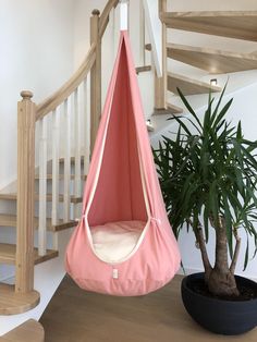 a pink hammock chair next to a potted plant on the floor in front of a spiral staircase