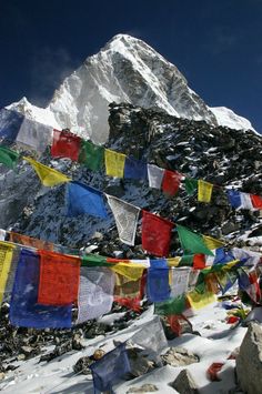 many colorful flags are hanging on the side of a snowy mountain with a snow capped peak in the background