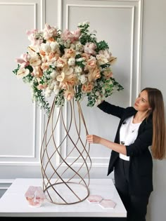 a woman standing next to a tall metal vase with flowers in it's center