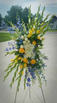 an arrangement of flowers is displayed on a tripod in front of a driveway area