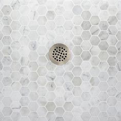 a white marble tiled shower wall with hexagonal holes in the middle and a metal grate on the side