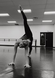 a woman is doing a handstand on the floor in an empty gym room