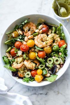 a white bowl filled with shrimp, tomatoes and avocado salad next to a cup of dressing