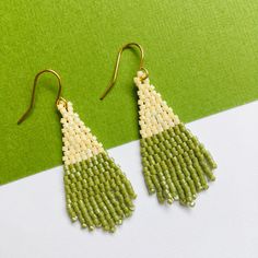 green and white beaded earrings sitting on top of a green table next to a pair of scissors