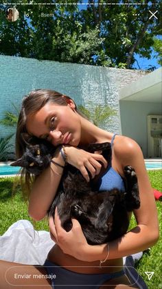 a woman holding a black cat in her arms and looking at the camera while sitting on grass