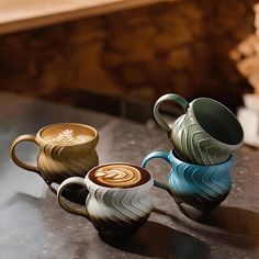 three coffee mugs sitting on top of a table next to each other with designs