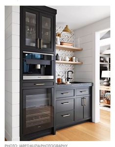 a kitchen with black cabinets and white tile backsplash, wood flooring and open shelving