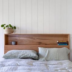 a bed with white linens and wooden headboard next to a potted plant