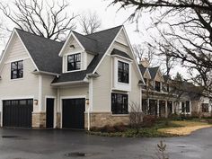 a large white house with black garage doors and windows on the top floor, surrounded by trees