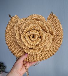 a hand holding a straw bag with a chain around the bottom and a flower design on it