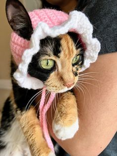 a cat wearing a pink and white knitted hat on it's head while being held by a woman