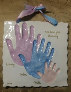 three handprints on a plaque with ribbon hanging from it's side, one is blue and the other is pink