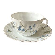 a white cup and saucer with blue flowers on it's rim, sitting next to each other