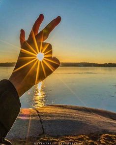 a person's hand is shown with the sun in the background and water behind them