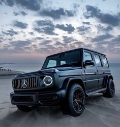 a mercedes g - class is parked in the sand at dusk on the beach near the ocean