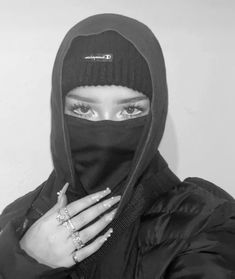 a woman wearing a black hood and holding her hands up to her face with one hand