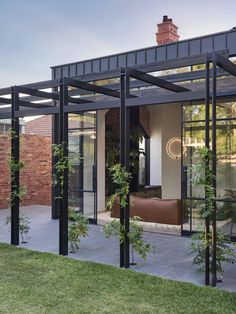 an outdoor living area with glass walls and black metal frame structure, surrounded by green grass