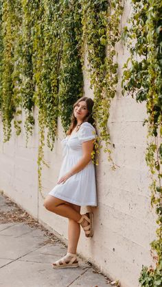 a woman leaning against a wall with ivy growing on it