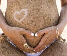 a woman holding sand in her hands with a heart drawn on it's stomach