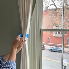 a person is opening the curtains in front of a window with a blue tape on it