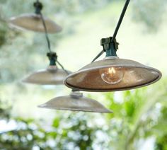 several lights hanging from a ceiling in front of a window with green plants behind them