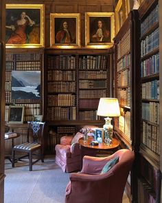 the library has many bookshelves and paintings on the walls, along with two chairs