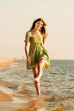 a woman in a green dress is running through the water at the beach on a sunny day