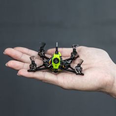 a person's hand holding a small green and black quadcopte with propellers