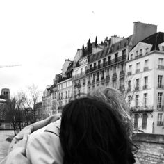 a woman standing in front of a river with buildings on both sides and birds flying overhead