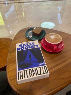 a cup of coffee and a book sitting on a table with a plate in front of it