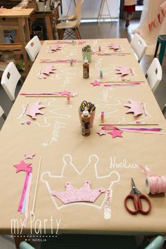 a table is decorated with pink and white paper crowns, stars, and other decorations