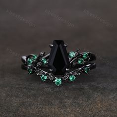 a black diamond ring with green stones on the sides and leaves around it, sitting on top of a table