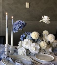 the table is set with blue and white flowers, plates, and candles on it