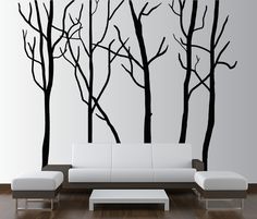 a living room with white couches and black trees on the wall behind it,