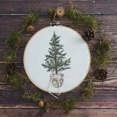 a cross stitch christmas tree on a wooden table with pine cones and twine around it