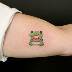 a person with a tattoo on their arm has a green frog holding a watermelon