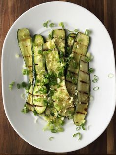 a white plate topped with sliced up zucchini and green onions on top of a wooden table