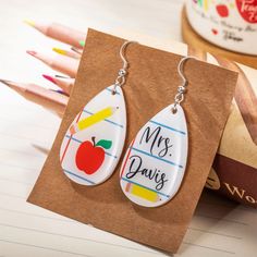 a pair of earrings with the words mrs davis written on them next to pencils