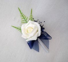 a white rose and blue ribbon boutonniere on a white surface with green leaves