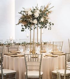 a tall centerpiece with white flowers and greenery sits on top of a round table