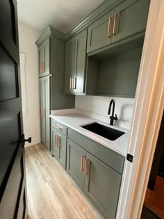 an empty kitchen with green cabinets and white counter tops, wood flooring in the foreground