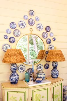 a blue and white cabinet with two lamps on top of it next to a round mirror