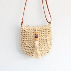 a straw bag hanging on the wall with a wooden bead and tasseled handle