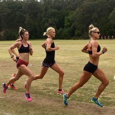 three women are running in a race on the grass with trees in the back ground