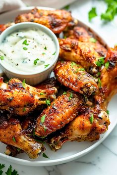 a white plate topped with chicken wings covered in ranch dressing and garnished with parsley