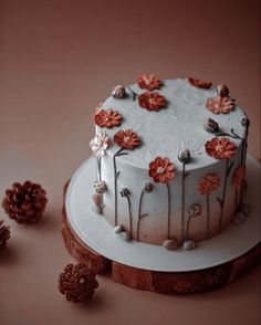 a white cake with flowers on it sitting on a table next to some pine cones