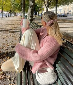 two women are sitting on a park bench and one is holding a cup in her hand