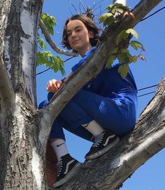 a woman sitting on top of a tree branch wearing blue sweatpants and black sneakers