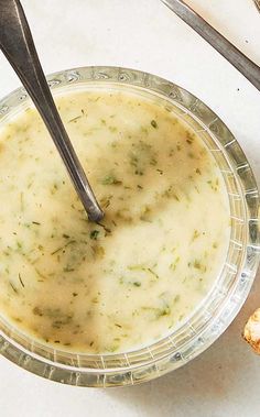 a bowl filled with soup next to two spoons on top of a white table