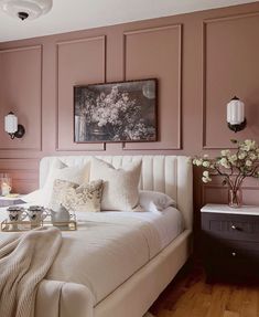 a bedroom with pink walls, white bedding and decorative artwork on the headboard